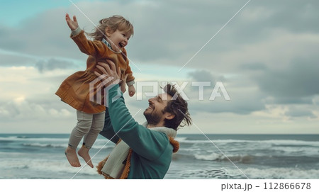 Joyful father lifting his child on a cloudy beach day. Candid family moment captured in a natural style. Perfect for sentimental projects. AI 112866678