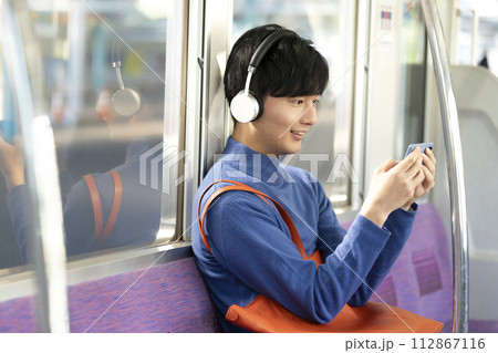 電車の中でスマートフォンを見る若い男性 112867116