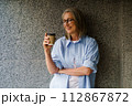 A woman wearing glasses stands holding a cup of coffee. 112867872