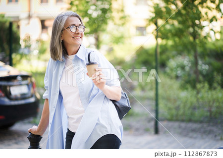 A woman is walking down a street, clutching a cup of coffee in her hand. 112867873