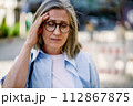A woman wearing glasses is shown holding her head in this straightforward image. 112867875