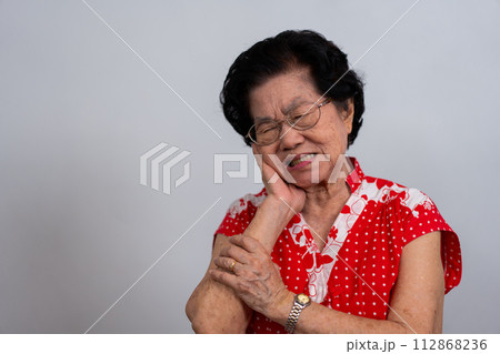 Asia old senior woman suffering from severe toothache, holding her cheek and suffering strong dental pain on white background, tooth decay, tooth sensitivity, oral health care concept. 112868236