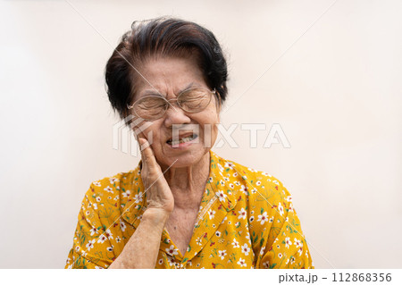 Asia old senior woman suffering from severe toothache, holding her cheek and suffering strong dental pain on white background, tooth decay, tooth sensitivity, oral health care concept. 112868356