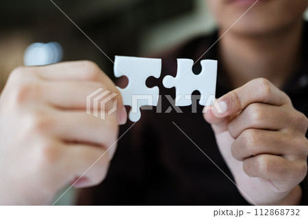 Two people holding a puzzle piece together. Concept of teamwork and collaboration. 112868732