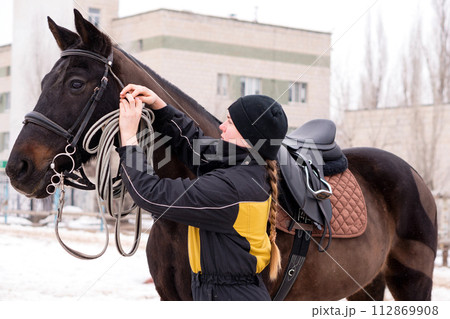 Person adjusting reins on saddled horse outdoors. 112869908