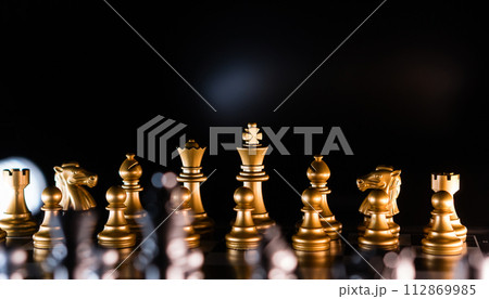 Golden chess pieces in dramatic backlighting Golden chess pieces in dramatic backlighting 112869985
