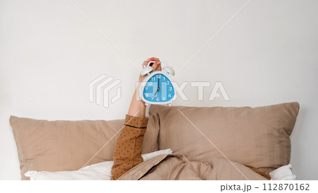 Hand holding alarm clock in bed Hand holding alarm clock in bed 112870162