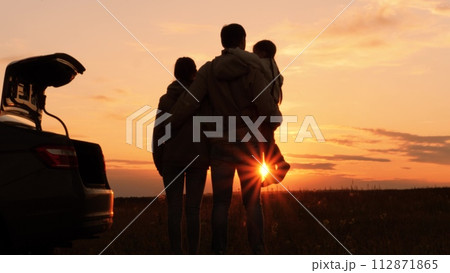 Silhouettes of happy family at sunset near car. Dad mom and girl kid watching contemplating setting sun, orange stunning summer sky. Solitude of family in nature, break from hustle and bustle of city Silhouettes of happy family at sunset near car. Dad mom and girl kid watching contemplating setting sun, orange stunning summer sky. Solitude of family in nature, break from hustle and bustle of city 112871865