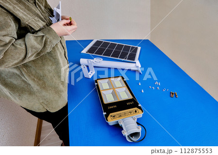 Green technology, solar energy for street lighting on private plot, woman installs an LED light and panel on mounting bracket. Green technology, solar energy for street lighting on private plot, woman installs an LED light and panel on mounting bracket. 112875553
