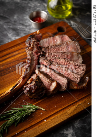 sliced tomahawk steak on wooden board 112875598