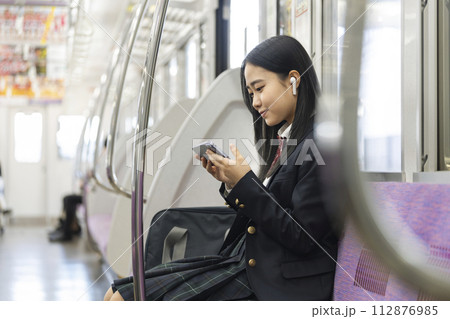 電車の中でスマートホンの画面を見るイヤホンをつけた女子高校生　電車通学　イメージ 112876985
