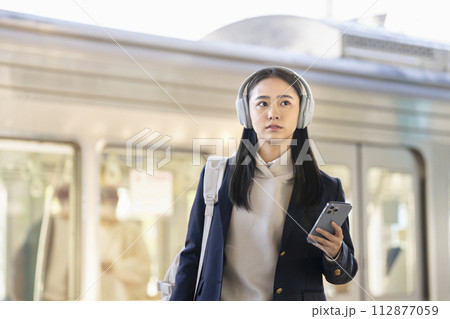 駅のホームを歩くヘッドホンをつけた女子高校生　　撮影協力「京王電鉄株式会社」 112877059