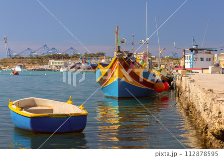 Multi-colored fishing boats luzzi with eyes in the harbor of the village Marsaxlokk on the island Malta. Multi-colored fishing boats luzzi with eyes in the harbor of the village Marsaxlokk on the island Malta. 112878595