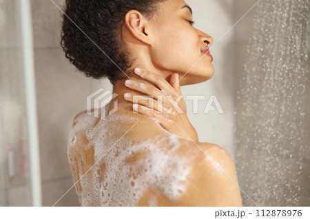 A woman lathers soap on her shoulder while taking a shower 112878976
