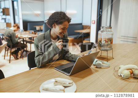 A woman sits at a desk with a laptop and coffee on a wooden table 112878981