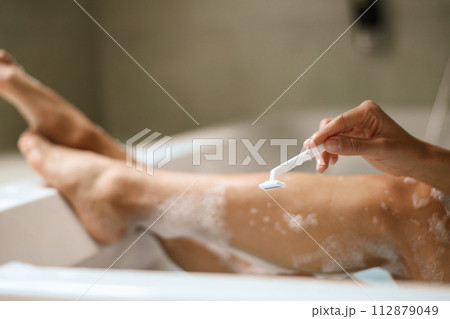 A woman is using a razor to shave her legs in a bathtub A woman is using a razor to shave her legs in a bathtub 112879049