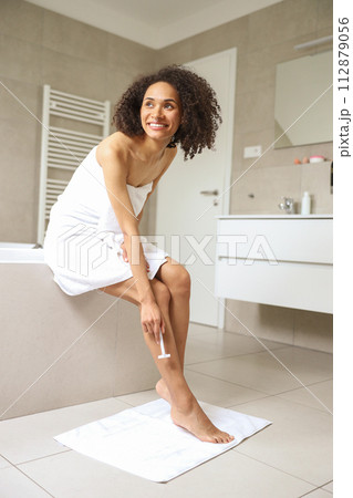 A woman is smiling while shaving her legs on the bathtub 112879056