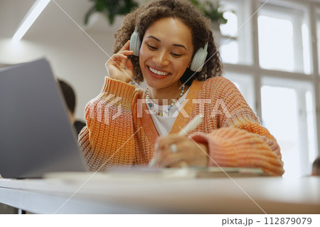 a woman wearing headphones is sitting at a table with a laptop and a pen 112879079