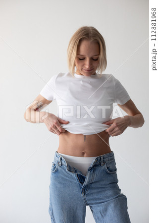 Beautiful blonde girl in a white T-shirt and blue jeans and sneakers posing on a white background Beautiful blonde girl in a white T-shirt and blue jeans and sneakers posing on a white background 112881968