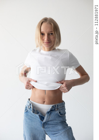 Beautiful blonde girl in a white T-shirt and blue jeans and sneakers posing on a white background 112881971