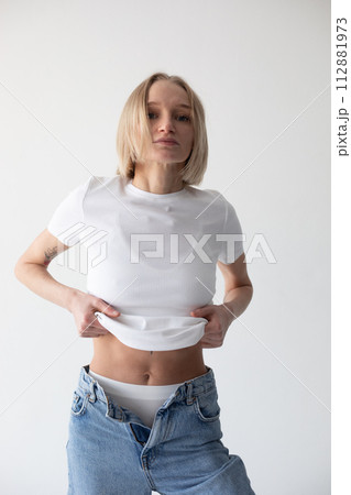 Beautiful blonde girl in a white T-shirt and blue jeans and sneakers posing on a white background Beautiful blonde girl in a white T-shirt and blue jeans and sneakers posing on a white background 112881973