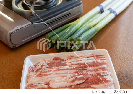 しゃぶしゃぶセットがテーブルに置かれている　カセットコンロと白ネギと豚肉のスライス 112885559
