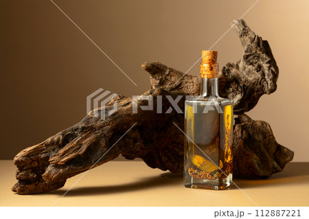 Bottle of spicy olive oil and olive tree snag on a beige background. Bottle of spicy olive oil and olive tree snag on a beige background. 112887221