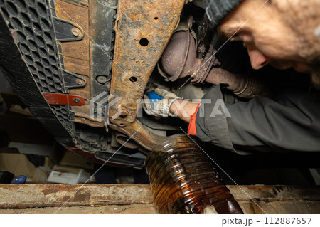 A mechanic repairs a car in a garage in a pit. A man replaces motor oil and filter in a car in the garage at home. Bottom view of the bottom of the car and changing the oil and filters. 112887657