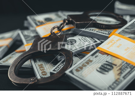 Close-up of handcuffs lying on top of dollars on a black background. Packs of dollars and handbrake boxes lie beautifully on a black background. Money fraud concept. Close-up of handcuffs lying on top of dollars on a black background. Packs of dollars and handbrake boxes lie beautifully on a black background. Money fraud concept. 112887671