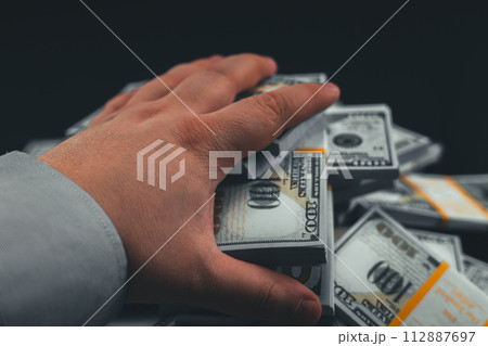 First person. A man reaches out and takes a wad of dollars from a pile on a table against a black background. Close-up. A hand reaches out and takes a wad of money from a table on a black background. First person. A man reaches out and takes a wad of dollars from a pile on a table against a black background. Close-up. A hand reaches out and takes a wad of money from a table on a black background. 112887697