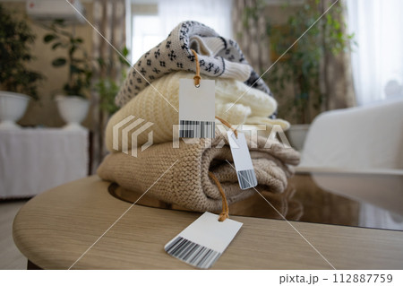While sorting out the clothes in the wardrobe, the woman put them in a pile on the table and attached tags for sale. Old clothes are reused by selling them on the Internet and second hand. While sorting out the clothes in the wardrobe, the woman put them in a pile on the table and attached tags for sale. Old clothes are reused by selling them on the Internet and second hand. 112887759