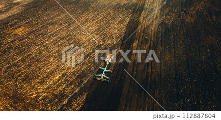 Aerial View. Tractor Plowing Field In Spring Season. Beginning Of Agricultural Spring Season. Cultivator Pulled By A Tractor In Countryside Rural Field Landscape Aerial View. Tractor Plowing Field In Spring Season. Beginning Of Agricultural Spring Season. Cultivator Pulled By A Tractor In Countryside Rural Field Landscape 112887804