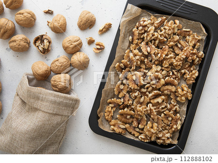 Baking tray with raw peeled walnut nuts and linen bag of whole nuts on light kitchen background. Baking tray with raw peeled walnut nuts and linen bag of whole nuts on light kitchen background. 112888102