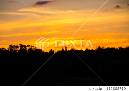 Orange sunset over silhouettes of village and trees 112888710