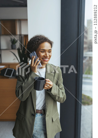 a woman is talking on a cell phone while holding a cup of coffee 112889212
