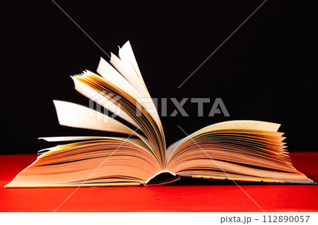 Pages of a thick book are turned on a red and black background. 112890057