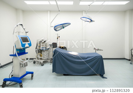 A typical operating room in a hospital with surgical light overhead for providing bright, directional lighting to the surgical team during procedure. The operating table is at the center of the room. 112891320