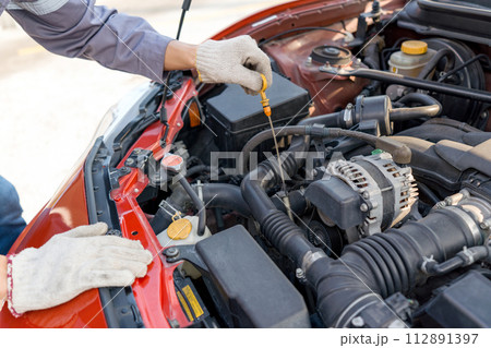 Closeup mechanic hand with protective glove checking the oil level of a car. Routine car maintenance for safe and efficient engine operation. Working atmosphere at car repair shop. Closeup mechanic hand with protective glove checking the oil level of a car. Routine car maintenance for safe and efficient engine operation. Working atmosphere at car repair shop. 112891397