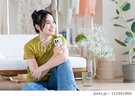 リビングでスマホを見る若い女性 112891966