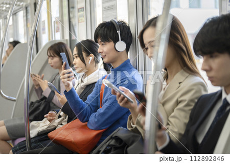 電車内の乗客 スマホの画面を見るヘッドホンをつけた若い男性 電車内の乗客 スマホの画面を見るヘッドホンをつけた若い男性 112892846