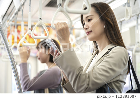 電車の中でスマートフォンの画面を見るイヤホンをしたビジネスウーマン 112893087