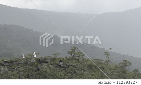 Hikers with White Raincoats Walking on Misty Mountain Ridge Hikers with White Raincoats Walking on Misty Mountain Ridge 112893227