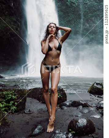 Woman in bikini with perfect body posing at waterfall in Bali. 112895625