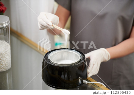 Beautician wearing gloves when mixing melted wax before applying on skin of client Beautician wearing gloves when mixing melted wax before applying on skin of client 112896430