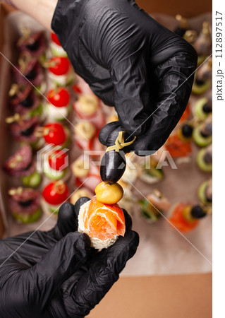 Canape, hands in black gloves hold a beautiful canape on a cap. Catering, snacking, food. Studio photo. Canape, hands in black gloves hold a beautiful canape on a cap. Catering, snacking, food. Studio photo. 112897517