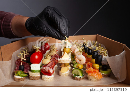 Canape, hands in black gloves hold a beautiful canape on a cap. Catering, snacking, food. Studio photo. Canape, hands in black gloves hold a beautiful canape on a cap. Catering, snacking, food. Studio photo. 112897519