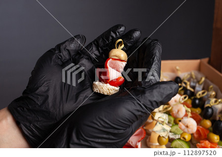 Canape, hands in black gloves hold a beautiful canape on a cap. Catering, snacking, food. Studio photo. 112897520