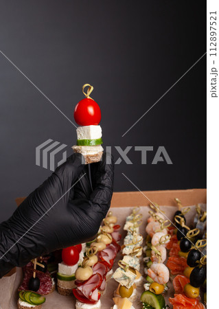 Canape, hands in black gloves hold a beautiful canape on a cap. Catering, snacking, food. Studio photo. Canape, hands in black gloves hold a beautiful canape on a cap. Catering, snacking, food. Studio photo. 112897521