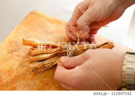 The man binds the grissini with an eco-friendly rope. A set of breadsticks. The man binds the grissini with an eco-friendly rope. A set of breadsticks. 112897582
