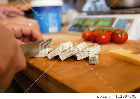 A woman cuts cheese with mold on a wooden board. In the background are scales 112897589